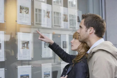 Couple looking in window outside estate agents Couple looking at houses in an estate agency window